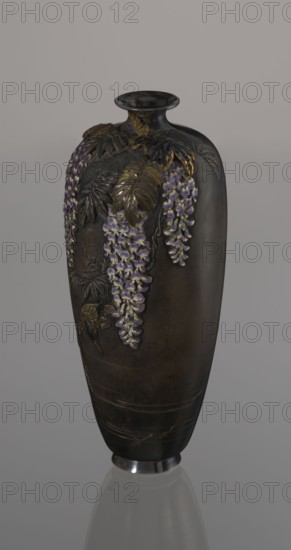 Vase, Toshitsugu craftsman. Meiji period 19th/20th century, Japan. Ovoid vase on a low ring foot with a very short neck and a strongly flaring, plate-like spout. Decorated in relief, applied, inlaid and engraved naturalistic motifs arranged asymmetrically: a wisteria vine with three clusters of flowers hanging down from the top near the neck; a kingfisher perches on a branch near the lowest flower, gazing into engraved water containing engraved fish. Decoration executed in the ro-iro zogan technique inlaid color painting, inlaying various metals and alloys and colored enamels white, several shades of lilac, subtle green accents. Leaves and bird figurine gilded and patinated with shakudo. Lower belly bears engraved inscription: Sumisuiin Toshitsugu sei. Vessel; height 16.2 cm, diameter 7.1 cm., A tall, narrow vase with a rounded shoulder and small flared neck, rendered in dark brown and black tones, decorated with a relief of hanging floral clusters in shades of purple and lilac and a f...