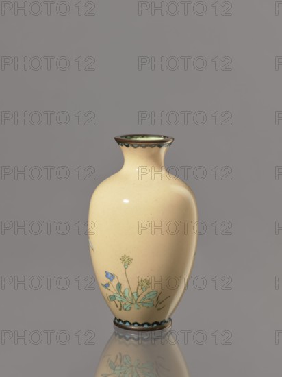 Vase, cloisonné enamel; Japan, Meiji period ca. 1900; vessel decorated with flowers and birds; height 12.2 cm, diameter 7.1 cm., A smooth ceramic vase with a pale yellow body and a narrow neck flaring at the rim, decorated near the lower side with a small floral motif showing leaves in green and flowers in blue and pale yellow, a scalloped dark trim at the rim and base, and a reflected image of the vase visible on the glossy surface beneath; background is a uniform gray.