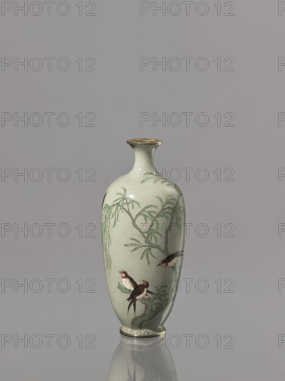 Vase with a short, thin, flared neck. Decoration: gray-green background with plants and swallows birds. Cloisonné enamel. Japan, Meiji period 1868–1912, 19th/20th century. Height 12.1 cm; diameter 5.3 cm., A slender ceramic vase with a pale green background sits upright against a gray backdrop, showing a glossy finish and a narrow neck with a slightly flared rim that has a metallic gold edge; the body of the vase is decorated with a painted scene in shades of green, brown, black, white, and red, depicting willow-like branches and leaves and a group of small birds perched on the branches, with darker green and brown tones for the branchwork and subtle shadowing where the vase curves, and the base of the vase has a decorative border and a faint reflection on the surface below.