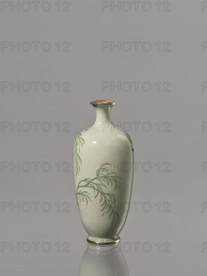 Vase with a short, thin, flared neck. Decoration with swallows and plants on a gray-green background. Cloisonné enamel, Japan, Meiji period 1868–1912, 19th/20th century. Vessel; height 12.1 cm, diameter 5.3 cm., Gifted and later repossessed Krakow., A smooth, pale green ceramic vase with a narrow neck and flared rim stands upright against a plain gray background, showing a glossy surface and a subtle reflective sheen; delicate green leafy branches are painted on its curved body, with thin brownish outlines accenting the foliage, and the rim and base have thin metallic-looking bands; the vase casts a faint reflection on the surface beneath it.