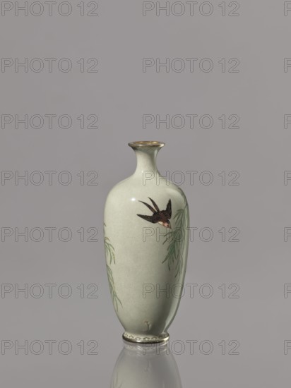Vase, Cloisonné enamel vase with a short, thin, flared neck. Decoration of swallows, plants, and birds on a gray-green background. Japan, Meiji period 1868–1912, late 19th/early 20th century. Vessel; height 12.1 cm, diameter 5.3 cm., A pale green ceramic vase with a narrow neck and flared rim stands against a neutral gray background, decorated with a painted dark brown and reddish bird in flight and slender green leafy branches on its curved surface, with a slightly reflective base and subtle glossy highlights.