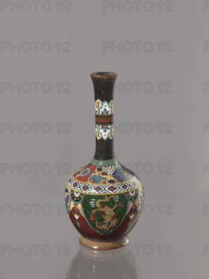 Vase, creator, gift; Japanese art; Meiji period 1868–1912, ca. 1900; Japan. Cloisonné enamel vessel decorated with birds, dragons, and phoenixes. Height 19.3 cm, width 8.9 cm., A tall narrow-necked vase with a bulbous base stands against a plain gray background; the neck is predominantly black with a subtle textured pattern and a horizontal band of decorative panels in white, blue, red, and yellow, while the rounded body features ornate multicolored designs including deep green panels with golden dragon-like figures, red fields, blue and white geometric borders, and accents of yellow and turquoise, all resting on a small decorated foot with reddish-brown and gold tones and showing a reflection on the smooth surface beneath.