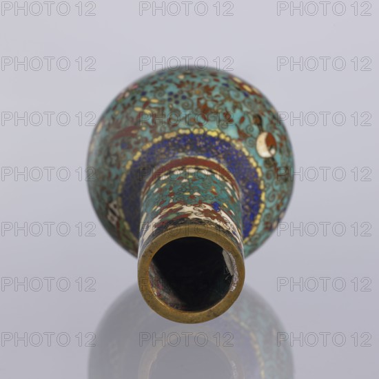 Vase, cloisonné enamel; Meiji period, ca. 1880; Japan, Nagoya. Vase with a spherical belly and a long cylindrical neck decorated over the entire surface with small floral and geometric motifs on a turquoise background. Height 9 cm; diameter 5.7 cm., A decorative cylindrical object viewed from its open end, showing an inner dark hollow and a rounded body decorated with intricate patterns; the surface displays a dominant turquoise color with accents of blue, green, red, white, gold, and brown, featuring swirling motifs and floral-like designs, and a metallic rim with a brass-like tone, all set against a pale gray background with a subtle reflection beneath the object.