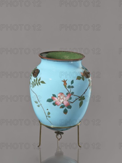 Vase, Japanese, Meiji–Taisho period ca. 1910–1920, cloisonné enamel, kachoga bird-and-flower design depicting flowers, wisteria, roses, and swallows; vessel, height 20 cm, diameter 15.3 cm., A light blue ceramic vase with a green interior rim sits on a thin brass stand; the vase features hand-painted floral motifs in pink and green with brown branches and small green leaves, and there are a few metal decorative rivet-like elements on its shoulder.