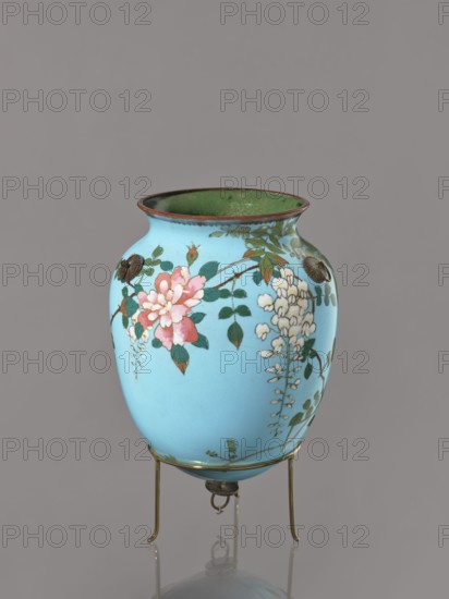 Vase, Japanese, Meiji–Taisho period ca. 1910–1920, cloisonné enamel, kachôga bird-and-flower motif depicting flowers, wisteria, roses, and swallows; vessel, height 20 cm, diameter 15.3 cm., A light blue rounded vase with a narrow flared rim, sitting on a small metal tripod stand; the vase has painted floral decoration including pink and white blossoms with green leaves and brown branches, and the interior of the rim appears green while the rim edge is a darker brownish color, the metal stand and fittings are a brass tone, and the background is a neutral gray.