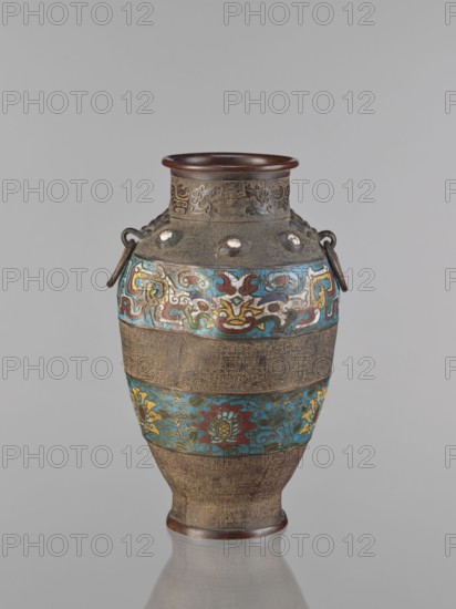 Vase, Chinese, Qing 1644–1911, 18th century, porcelain vessel decorated with lotuses, plant motifs, lotus tendril ornament, dragons and taotie iconography, height 30.5 cm, China., A tall ornamental vessel with a rounded body and narrow base, featuring an upturned rim and a pair of small looped handles with metal rings, shown against a plain light gray background. The vessel displays a textured brown surface with bands of intricate raised patterns and a few rounded protrusions near the neck. Decorative horizontal bands encircle the body with colorful motifs in turquoise blue, deep red, yellow, green, and white forming stylized floral and abstract designs, while the intervening bands remain primarily brown with fine carved details. The rim and base exhibit a darker brown finish.