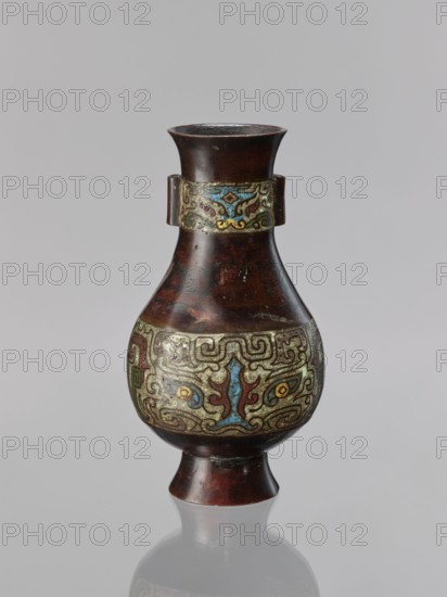 Vase, Chinese, taotie iconography, Qing dynasty 1644–1911, 19th century, ceremonial/ritual vessel, vessel, height 24 cm, diameter 13.1 cm., A dark reddish-brown vase with a flared mouth and a tapered neck sits against a pale gray background, featuring a decorative band near the neck and a wider ornate band around the bulbous midsection with swirling abstract patterns in blue, yellow, red, green, and pale gold; the surface shows areas of darker and lighter reddish-brown patina and slight wear, and the vase rests on a short pedestal foot that mirrors the reddish-brown color, with a subtle reflection beneath it.