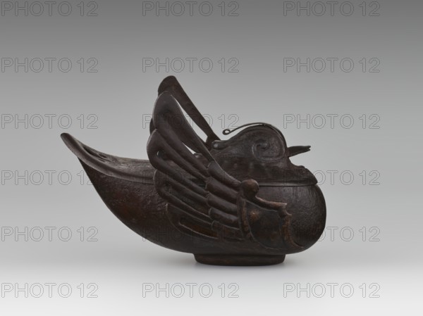 Duck incense burner, attributed to an, Chinese, Qing dynasty 1644–1911, 19th century. Ceramic vessel in the form of a duck with wings, function: incense burner. Dimensions: height 9.7 cm, width 13.6 cm. Subjects: ducks, birds. Provenance unknown., A dark brown sculpted object resembling a vessel with a curved hull and a raised rounded front is shown against a gray background. The vessel has a wing-like decorative element on its side with layered feather shapes and a prominent curved handle or strap rising from the center. The front section features a rounded lid with a small protruding beak-like extension and a curled motif on its surface. The surface appears textured and slightly worn, showing variations of dark brown and near-black tones with subtle highlights. The background shows a gradient of gray.