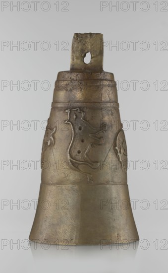 Bell, Islamic art, Persian Qajar dynasty, 1785–1925, 19th century, Iran; figurative motifs: animals, lions, camels, deer; painted/decorated bell; height 26.5 cm, diameter 15.0 cm., A single bell-shaped metal object stands upright against a pale gray background, showing a weathered surface with hues of bronze, gold, and muted brown; the top has a rectangular loop with a rough hole and darker brown patina, and the upper body features a few horizontal bands and textured wear; the midsection bears a raised decorative motif resembling stylized animal shapes in slightly darker bronze tones with pitted surface details; the lower flared portion is smoother with visible fine striations and a mix of dull bronze and gold coloration, and the object casts a subtle reflection on the glossy surface beneath it.