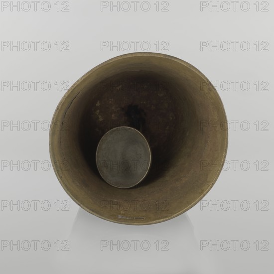 Bell, Islamic art, Persian, Qajar dynasty 1785–1925, figurative motifs, animals, lions, camels, deer, 19th century, Iran, varia, height 26.5 cm, diameter 15.0 cm, A large metallic bell viewed from above showing its circular rim and hollow interior with a suspended round clapper; the bell surface has a worn, mottled appearance in shades of brown and dark brown with areas of darker patina, and the background is a smooth light gray.