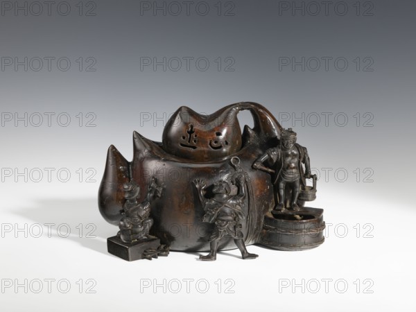 Censer kôro, figurative scenes, Japanese art, gourds, Japanese, Meiji 1868–1912, bronzes. Decorated with figurines of Japanese people busy scrubbing its surface. Incense burner in the shape of a leather cistern, 2nd half of the 19th century, Japan; vessel, censer; height 16.3 cm, width 26.5 cm., A dark brown carved object with a glossy surface sits on a pale surface against a gray background. The main form has a rounded, bulbous body with several pointed protrusions and a handle-like arch on one side. A group of small sculpted figures in similar dark brown material are arranged around the base: one figure stands on a small rectangular block, another stands with arms raised in front of the main body, and a third stands on a circular stepped platform holding a pail. The sculpture shows varied textures with smooth rounded areas, carved details on the figures' clothing and faces, and some lighter brown highlights where the surface appears worn. The overall colors visible are dark brown, li...