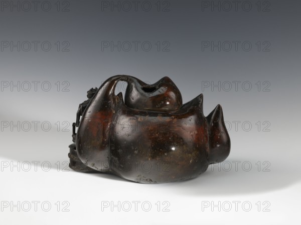 Censer kôro, figurative scenes, Japanese art, gourds, Japanese, Meiji 1868–1912, bronzes. Decorated with figurines of Japanese people busy scrubbing its surface. Incense burner in the shape of a leather cistern, 2nd half of the 19th century, Japan, vessel, censer; height 16.3 cm, width 26.5 cm, A dark brown, glossy carved object with a rounded, organic form resembling a group of bulbous shapes fused together sits on a light surface against a neutral gray background; the object shows areas of rich reddish-brown and black patina with some worn, lighter spots and subtle greenish tints, and features smooth contours, pointed protrusions, and a curved handle-like arch on top with an opening, while a few small carved details extend from one side.