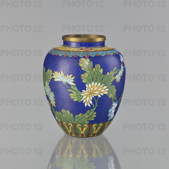 Vase, cloisonné enamel, Chinese art; ornament: plants peonies and meander motif; oval-shaped vase with a short neck and ring-shaped spout, without a foot; decorated on the central belly with colorful flowers on a sapphire background and with a Chinese meander motif; Qing dynasty 1644–1911, 19th century; China; vessel; height 16.5 cm, diameter 13.8 cm, A rounded vase with a narrow gold rim sits against a neutral gray background, predominantly covered in a deep cobalt blue field patterned with an intricate geometric design; the vase is decorated with a group of floral motifs showing several white and pale yellow flowers with layered petals and green leaves, along with accents of light blue and pale pink blossoms, a decorative band near the top featuring turquoise and gold scalloped motifs, and a border at the base with green and red ornamental shapes; the surface shows a subtle reflection of the vase on the glossy ground.