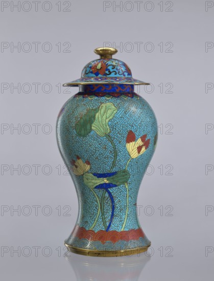 Vase with cover;, Cloisonné enamel vessel decorated with lotuses and geometric patterns. Qing dynasty 18th century, China. Height: 37 cm., A lidded vase with a bulbous body and flared foot rendered in turquoise, blue, green, red, gold, and cream tones; the surface is decorated with a repeating maze-like pattern in blue on a turquoise ground and stylized botanical motifs including large green leaves and cream and red flower heads with blue stems; the domed lid has a wide, flat rim with ornate blue and red scrollwork and a gold finial, and a band of red scalloped decoration runs above the foot; the base and finial show metallic gold accents, and the object sits against a neutral pale gray background.