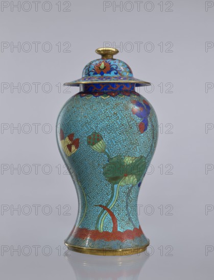 Vase with cover, Chinese, Qing dynasty 1644–1911, cloisonné enamel, decorated with lotuses and geometric patterns, decorative vessel/vase, 18th century China, height 37 cm., The image shows a lidded vase with a bulbous body tapering to a narrower base, decorated in a dominant turquoise color with an intricate repeating geometric pattern, accented by a few green lotus leaves and stems, several red and yellow lotus buds, and some purple and blue floral elements; the lid and rim feature bands of deep blue with red and gold decorative motifs, and the finial, rim edge, and base edge are metallic gold.