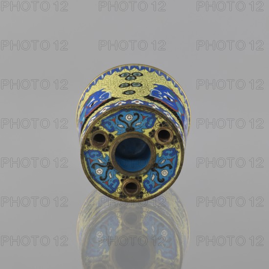 Sawdust container, cloisonné enamel vessel, 19th century China Qing dynasty, height 8.5 cm, diameter 9.7 cm. Decoration on a yellow ground: base with four inserts and four masks against a grid background; motifs include beasts fantasy, tiger symbol, and meander ornament., A cylindrical object lies on a reflective surface, shown from an end-on perspective; the visible end has a central hollow circled by a metallic rim and three smaller circular openings around it, and the surface of the cylinder is decorated with ornate enamel patterns in blue, yellow, and touches of black and white, with additional accents of green and red visible in the design; the background is a uniform light gray and the object’s colorful decoration is mirrored faintly on the surface below.