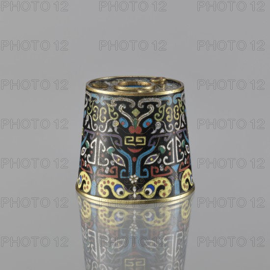 Sawdust container, gift, Paderewski, Ignacy Jan 1860-1941, Chinese art, Chinese, Qing dynasty 1644–1911, cloisonné enamel, fantasy beasts, cicadas, base with four inserts, 19th century, China, vessel; height 8.5 cm, diameter 9.7 cm, A small conical metal object sits upright on a reflective surface, showing a colorful enamel pattern against a black background with a gold rim at the top and bottom. The surface features ornate swirling motifs and stylized shapes in colors including blue, red, yellow, green, white, and purple. The design includes symmetrical, mask-like forms and curving decorative elements that repeat around the object. The reflection of the object is visible on the surface below, mirroring the same colors and patterns. The background is a plain gray.