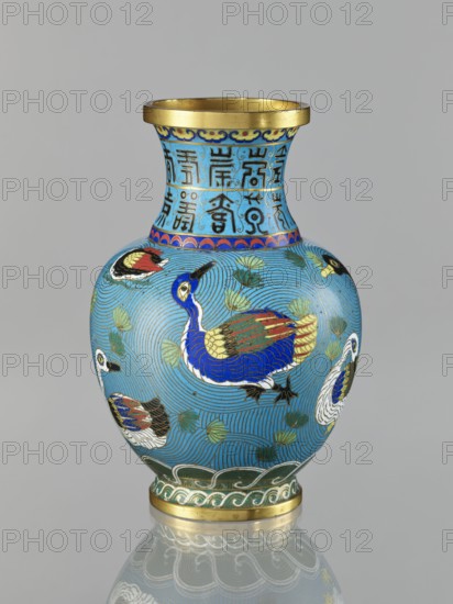 Vase, Chinese, Qing 1644–1911, cloisonné enamel, 19th century. Vase on a foot with a neck; decoration: ducks on a turquoise background and an archaizing inscription on the neck; iconography includes longevity shou; height 23.3 cm; vessel., A ceramic vase against a neutral gray background with a bright turquoise-blue ground decorated with a group of stylized ducks in vivid colors, including deep blue, red, white, green, gold, black, and yellow; the body shows swirling linear patterns in a slightly darker turquoise with green leaf-like motifs, and several ducks rendered with layered feathers in blue, red, gold, white, and black; the neck features a band with ornamental motifs in turquoise, blue, black, and gold beneath a gold rim, and the foot is bordered with a green and gold wave pattern above a gold base that reflects faintly on the surface below.