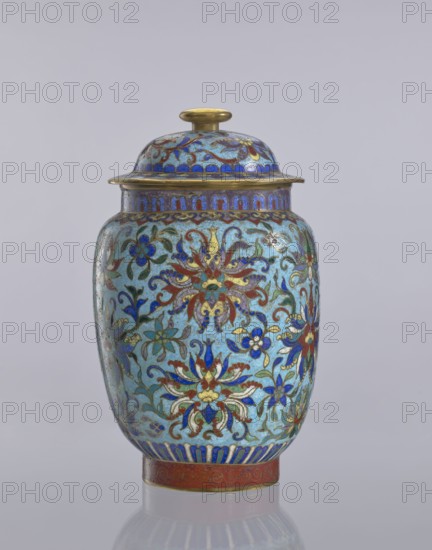 Vase with lid, Chinese, Qing 1644–1911, cloisonné enamel decorative vessel with floral ornaments, flowers, plant and lotus tendrils, 18th–19th century, China; height 23 cm, diameter 14 cm., A lidded jar with a rounded body and a domed top sits against a pale gray background, decorated with an intricate floral pattern in shades of blue, turquoise, red, green, gold, and white, with gold-colored metal edging on the lid and rim and a gold-colored knob on top; the body shows several stylized flowers and scrolling vine motifs in blue, red, green, and gold on a light turquoise ground, with a band of blue and gold patterning near the base and a red and gold band at the foot.