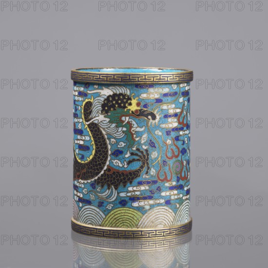 Brush vessel, 19th century China, Qing dynasty; cloisonné enamel decorated with dragons, clouds, waves, claws, and meander ornament; turquoise interior; height 12.7 cm, diameter 9.8 cm; used for brushes., A cylindrical decorative vessel with a glossy surface showing a stylized dragon motif in a palette of turquoise blue, deep blue, black, gold, white, red, green, and touches of yellow and purple; the dragon is rendered with black scaled body and gold outlines, a head with white and yellow detailing and red accents, surrounded by swirling cloud-like forms in white and blue and flame-like shapes in red and gold; the vessel has patterned gold and blue bands at the top and bottom edges and a repeating wave pattern near the base in shades of green, white, and gold; the object sits on a reflective surface and is set against a neutral gray background.