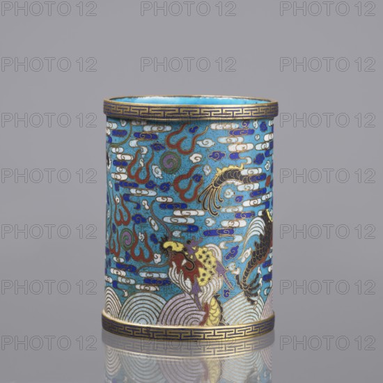 Brush vessel, Chinese, Qing dynasty 1644–1911, cloisonné enamel with dragon and cloud decoration, waves/sea waves, claws, meander ornament, turquoise interior; 19th century, China; height 12.7 cm, diameter 9.8 cm., A cylindrical decorative object with a dominant turquoise-blue background covered in intricate cloisonné patterns in colors including blue, white, red, green, gold, black, purple, and yellow, featuring cloud-like motifs, swirling lines, and stylized fish or bird figures, with a gold band with a geometric border at the top and bottom, and a reflective surface beneath it showing a soft mirrored outline.
