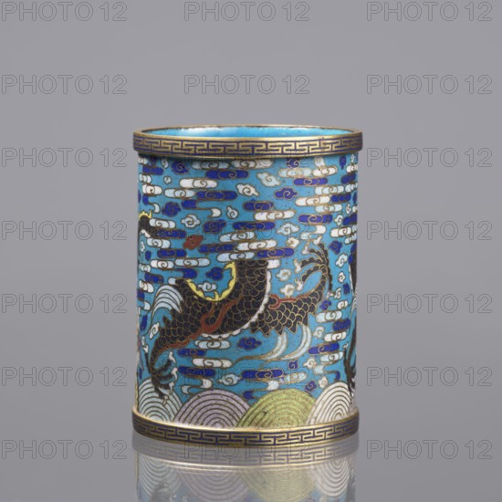 Brush vessel; Chinese; Qing dynasty 1644–1911; cloisonné enamel decorated with dragons, clouds, waves, claws, and meander ornament; turquoise interior; 19th century; height 12.7 cm, diameter 9.8 cm., A cylindrical decorative object with a glossy surface featuring a predominantly turquoise blue background, decorated with a pattern of cloud-like shapes in white and deep blue, and several stylized fish or dragon-like creatures in dark brown and black with gold and red accents; the top and bottom rims have a narrow band with a repeating geometric motif in gold and dark blue, and the lower edge shows layered wave patterns in pale green, cream, and muted gold; the overall color palette includes turquoise, deep blue, white, dark brown, black, gold, red, pale green, and cream, and the object is shown against a smooth gray background with a faint reflective surface beneath it.