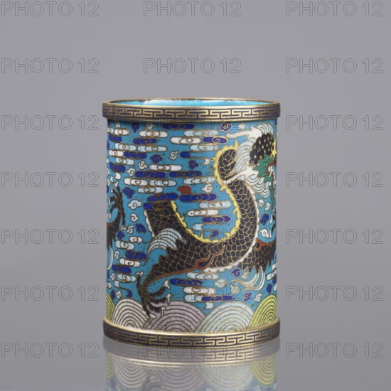 Brush vessel;, gift; Paderewski, Ignacy Jan 1860-1941; Chinese; Qing dynasty 1644–1911; cloisonné enamel; 19th century, China. Decoration: dragons, clouds, waves/sea waves, claws, meander ornament. Function: brush vessel. Turquoise interior. Height 12.7 cm; diameter 9.8 cm., A cylindrical decorative object with a blue background showing a stylized fish or dragon motif in dark brown and gold with white fins, set among cloud-like shapes in white, blue, and purple; the top and bottom rims have a patterned band in gold and dark blue; the lower edge shows wave-like bands in pale yellow, green, and white; the overall colors visible include blue, gold, dark brown, white, purple, green, and pale yellow, and the object rests on a reflective surface with a neutral gray background.