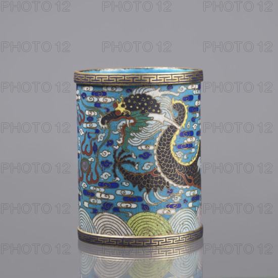 Brush vessel, 19th century, China; Qing dynasty; cloisonné enamel; subject: dragons, clouds, waves, claws, meander ornament; function: brush vessel; turquoise interior; height 12.7 cm, diameter 9.8 cm., A cylindrical decorative object shown upright with a glossy surface, featuring a dominant turquoise blue background and detailed cloisonné-style enamel work. The central area displays a stylized dragon or serpentine creature rendered in black, dark brown, green, white, red, and gold outlines, with flowing mane-like shapes and scale patterns. Surrounding the creature are swirling cloud and wave motifs in white, blue, dark blue, and touches of red and green. The top and bottom rims have a repeating geometric border in gold on a blue band. The lower section includes scalloped wave patterns in pale green, white, and light blue with gold accents. The overall palette includes turquoise blue, dark blue, white, black, gold, green, red, and brown, and the piece sits against a neutral gray backgr...