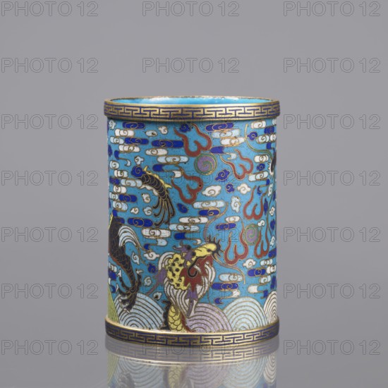 Brush vessel, cloisonné enamel, Qing dynasty 1644–1911, 19th century, China. Decorated with dragons, clouds, waves/sea waves, claws, and meander ornament; turquoise interior. Function: brush vessel. Height 12.7 cm; diameter 9.8 cm., A cylindrical object with a glossy surface sits against a neutral gray background, decorated all over with a bright turquoise base and patterns in blue, white, red, gold, black, purple, and green; the decoration includes cloud-like motifs and flame shapes, stylized waves at the bottom, and a few serpent- or dragon-like figures with scaly bodies and flowing manes, all outlined and detailed in gold; a geometric gold band runs along the top and bottom edges, and the piece reflects softly on the surface beneath it.