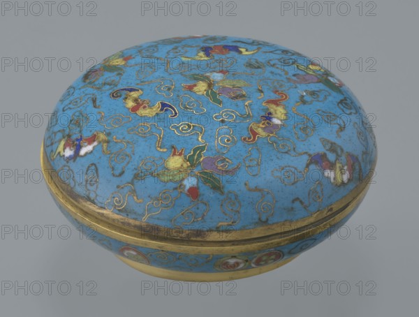 Round box with a lid, cloisonné enamel, Chinese, Qing 1644–1911. Cylindrical, flattened in shape, on a separate ring foot, with a slightly convex lid. Entire surface decorated with multicolored lotus tendrils on a turquoise background. Lid shows three fruits—peach, pomegranate, and lemon—and accompanying bats, an auspicious motif interpreted as many happiness, long life, and many sons. Background composed of cloud motifs formed from bent wire. Interior storage section decorated with colorful medallions single, paired, or triple featuring various Chinese plant ornaments. Rounded edges of lid and storage section, lower edge of foot and bottom gilded. Bottom and entire interior covered with turquoise enamel. 19th century, China. Height 4.6 cm; diameter 9.8 cm., A rounded lidded container with a domed top, covered in a bright blue enamel decorated with a pattern of swirling cloud-like motifs traced in gold and accented with a few multicolored floral and bat-like shapes in red, green, purpl...