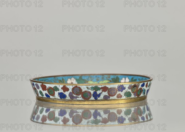 Plate with a brim; cloisonné enamel dish with plant ornaments and a tiger symbol. Chinese, Qing dynasty 1644–1911, 19th century. Height 2.4 cm; diameter 14.2 cm., A low, shallow dish with a metallic rim and base band decorated with enamel in a repeating pattern of round and cloudlike shapes in colors including turquoise, blue, green, red, purple, and white, with an inner surface showing a bright turquoise background and floral motifs in green and white; the dish rests on a reflective surface that mirrors its patterned side, and the background is a pale neutral gray.
