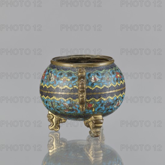 Ding incense burner, Paderewski, Ignacy Jan 1860–1941, Chinese, Qing dynasty 1644–1911, cloisonné enamel ceremonial vessel decorated with floral motifs, butterflies, peonies, and fantasy beasts. Ding incense burner on a tripod with two plastically shaped handles, no cover. Floral decoration in striped arrangements. 18th century, China. Vessel; height 8.4 cm, width 12.4 cm, diameter 9.8 cm., A small rounded vessel sits on a reflective surface, supported by a group of ornate tripod feet in a metallic gold color; the body of the vessel is covered in an intricate cloisonné-like pattern predominantly in shades of bright turquoise blue and deep navy blue with accents of gold, red, white, and pale yellow, and it has a metallic gold rim and a vertical handle-like decorative element in gold on the front.