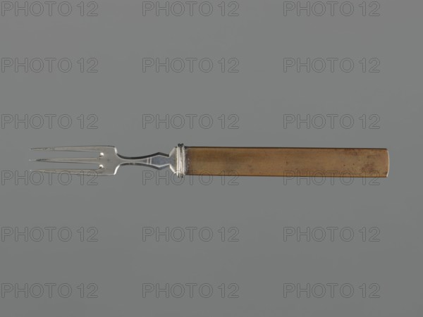 Fork with knife handle kozuka, Japanese, Edo period 1603–1868, 18th century, kozuka for katana, melee weapons/sword fitting, fork/cutlery, height 16.9 cm, width 1.4 cm., A single fork is shown horizontally against a solid gray background, with a metallic silver three-pronged tine section on the left transitioning to a short decorative silver neck and a long rectangular handle in a tarnished brownish-gold color; the silver parts show reflective highlights and slight wear, and the brownish-gold handle shows uneven coloration and subtle spots of darker discoloration.