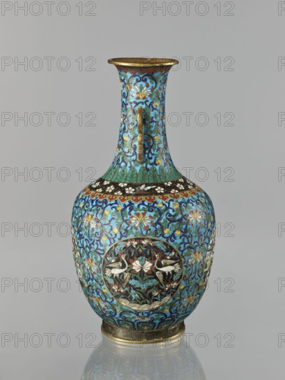 Vase, Qing dynasty 1644–1911, 19th century, China. Cloisonné enamel vase with neck; decoration of lotuses, peonies, chrysanthemums, lotus tendril ornament, meander ornament, cranes, deer, tigers, other zoomorphic motifs, and birds and animals depicted in circular medallions on a turquoise plant-background. Two stylized handles on the sides of the neck. Height 33.0 cm, diameter 15.0 cm, weight 1.7 kg., A decorative vase with a flared rim and a long neck that widens into a rounded body, featuring a handle on the neck; the surface is covered in intricate floral and foliate patterns in shades of turquoise, light blue, dark blue, green, black, white, red, gold, and brown; several circular medallions on the body contain stylized birds and lotus motifs in white, black, red, and green against dark backgrounds, surrounded by scrolling blue and turquoise arabesques and small floral elements; a band of repeating geometric motifs in gold and brown encircles the base, and a narrow band with floral ...