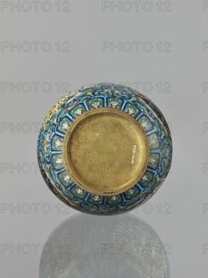 Vase, Chinese, Qing dynasty 1644–1911, 19th century. Cloisonné enamel vessel with a neck, height 33.0 cm, diameter 15.0 cm, weight 1.7 kg. Decoration: floral and plant tendrils on a turquoise background; lotuses, peonies, chrysanthemums; lotus tendril ornament and meander ornament; birds, cranes, deer, tigers and other zoomorphic motifs in circular medallions on a plant background. Two stylized handles on the sides of the neck., A round, ornate bowl shown from above with an unadorned central interior in a metallic gold tone, surrounded by a richly patterned exterior band featuring a repeating motif in shades of blue, turquoise, teal, white, dark blue, and touches of red and yellow, against a neutral gray background and a faint reflective surface beneath that shows a muted, mirroring impression of the bowl.
