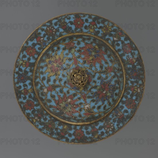 Tin with a lid, Chinese, Qing dynasty, Qianlong period, 18th century. Cylindrical tin with a wide plate-like collar extending beyond the vessel walls and slightly rising at the rim. Domed lid with a handle in the shape of a decorative knob with openwork relief: a dragon in clouds, its head directed toward a pearl at the top of the handle. Exterior of the vessel box and collar decorated in cloisonné enamel with a multicolored red, blue, green, yellow, white small-flowered ornament — branches with rosettes, buds, and leaves — on a turquoise background. Lid decorated with a lotus tendril of four geometrically arranged flowers and surrounding branches; a multi-petal rosette at the center under the metal handle, all on a turquoise ground. Bottom filled with a rich multicolored composition of elements reminiscent of Buddhist symbols — a vajra and Dharma wheel forming the inner central rosette, with red and blue ribbons between the symbols. Interior of box and lid ungilded of enamel; all inte...