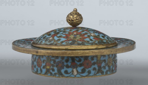 Tin with a lid, Paderewski, Ignacy Jan 1860–1941, Chinese, Qing 1644–1911, Qianlong period, cloisonné enamel. Cylindrical tin with a wide plate-like collar extending beyond the vessel walls, slightly rising at the rim. Domed lid with a handle shaped as a decorative openwork relief: a dragon in clouds, head directed toward a pearl atop the handle. Exterior box and collar decorated with a multicolored red, blue, green, yellow, white small-flowered ornament — branches with rosettes, buds, and leaves — on a turquoise background. Lid decorated with a lotus tendril of four geometrically arranged flowers and surrounding branches; center beneath the metal handle features a multi-petal rosette, also on turquoise. Bottom filled with a rich multicolored composition of elements reminiscent of Buddhist symbols — a vajra and Dharma wheel forming the inner central rosette, with two-colored red and blue ribbons between the symbols. Interior of box and lid lacks enamel decoration; all interior elements...