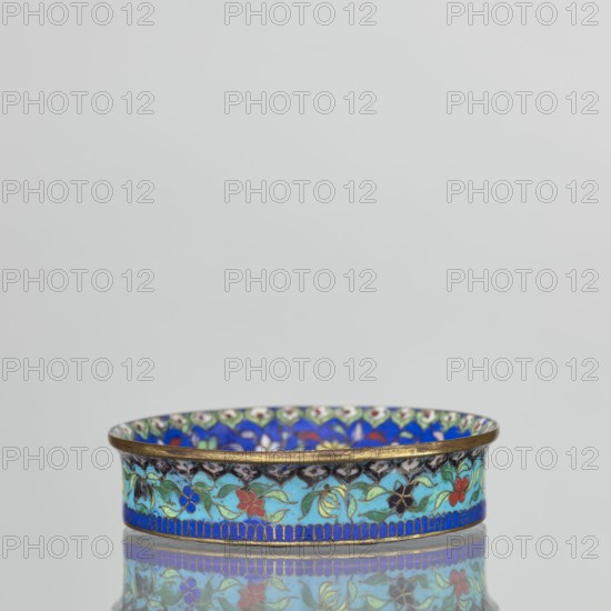 Bowl, Chinese, Qing dynasty 1644–1911, cloisonné enamel decorative vessel depicting flowers and butterflies. Decoration: inside bottom decorated with flowers on a light lilac background; collar decorated with flowers on a sapphire background; outside the collar decorated with flowers on a turquoise background; bottom covered with lilac enamel. 19th century, China. Height 2.3 cm; diameter 9.5 cm., A shallow round dish with a thin metallic rim sits centered against a pale gray background, its exterior decorated with a repeating floral pattern in turquoise, blue, red, green, black, and gold tones, and a band of darker blue along the base; the interior edge shows a similar colorful motif with prominent blue and green areas, and the dish and its pattern are reflected on the glossy surface beneath it.