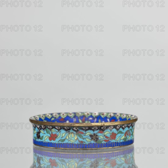 Bowl, maker, 19th century, China; Qing dynasty. Cloisonné enamel decorative vessel, height 2.3 cm, diameter 9.5 cm. Decoration: inside the bottom decorated with flowers on a light lilac background; collar decorated with flowers on a sapphire background; outside the collar decorated with flowers on a turquoise background; bottom covered with lilac enamel. Subject: flowers and butterflies., A shallow round dish with an ornate floral band around its side, showing a repeated pattern of stylized flowers and leaves in colors including blue, turquoise, green, red, black, gold, and a hint of white, with a gold rim and a narrow blue border along the bottom edge, set against a plain light gray background and reflected faintly on the surface beneath it.