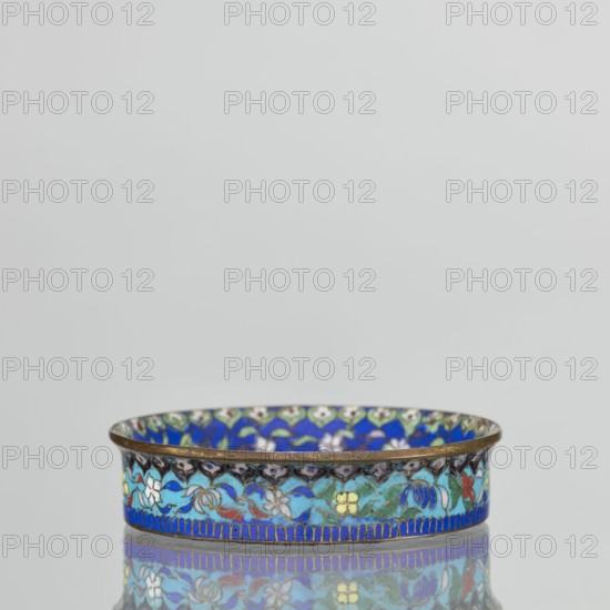 Bowl, gift, Chinese, Qing dynasty 1644–1911, cloisonné enamel decorative vessel, 19th century, China; vessel, height 2.3 cm, diameter 9.4 cm. The round, flat-bottomed bowl with a low side wall widening toward the rim is decorated in the mirror with an ornamental composition on a light purple background arranged around a central black rosette. The composition features four butterflies in white, red, and black, multicolored flowers including Buddha's fingers/Chinese lemon and surrounding leaves arranged in a circle. The inner wall is decorated with a floral tendril against a blue background with multicolored flowers similar to those in the mirror. A lambrequin ornament is visible at the edge, reminiscent of the shape of rui heads. The rim is curved outward and gilded. The turquoise outer wall is filled with decoration similar to that on the inner wall. The underside of the bottom is covered with a single-color purple enamel. This piece is a pair with another bowl., A shallow round dish w...