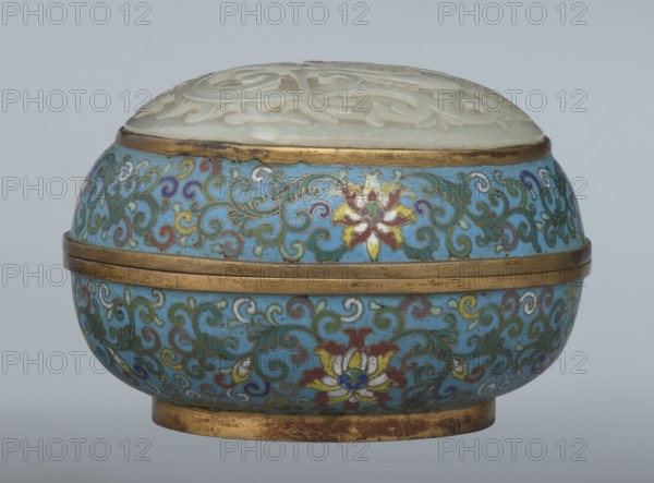 Box with a lid, Chinese, Qing dynasty 1644–1911, Qianlong period, cloisonné enamel; oval spheroidal box based on a ring foot, divided halfway into container and lid. Slightly convex bas-relief grayish jade plaque on the lid depicting a fenghuang phoenix or peacock with a sun among clouds; sun in upper left surrounded by a silk ribbon. Motifs and styling reference emblems from mandarin squares: peacock denoting third civil rank and sun referring to imperial authority. The jade plaque is a fine example of hard-stone workmanship. Rounded sides of container and lid decorated with multi-colored lotus tendril stripes on a turquoise ground. Interior filled with a uniform layer of turquoise enamel. Metal rings reinforcing the edges of the container, lid, and plaque attachment are gilded. 18th century, China. Height 8.2 cm; width 11.3 cm; diameter 12.2 cm., A rounded decorative container with a domed carved lid sits against a plain pale gray background; the lid appears off-white or cream with c...