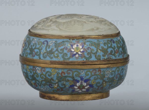 Box with a lid; maker, Chinese art; Qing dynasty 1644–1911, Qianlong period; cloisonné enamel. Oval, spheroidal box on a ring foot, divided halfway into container and lid. Slightly convex bas-relief plaque of grayish jade on the cover depicting a fenghuang phoenix or peacock with a sun among clouds; the sun is in the upper left surrounded by a silk ribbon. Motifs and styling refer to emblems on mandarin squares: peacock indicating third civil rank and the sun referring to imperial authority. The jade plaque is an exceptionally fine example of workmanship. Rounded sides of both container and lid decorated with a multi-colored lotus tendril stripe on a turquoise background. Interior filled with a uniform layer of turquoise enamel. Metal rings reinforcing the edges of the container, lid, and plaque attachment are gilded. 18th century, China. Height 8.2 cm; width 11.3 cm; diameter 12.2 cm., A round decorative box with a domed lid carved from pale cream material sits on a short circular bas...