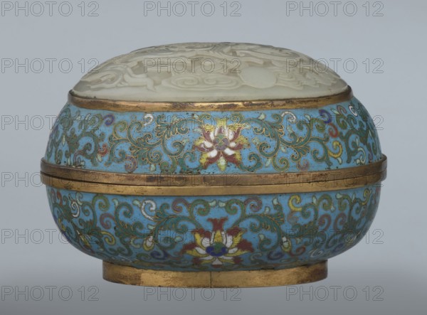 Box with a lid, cloisonné enamel, 18th century, China. Oval, spheroidal box on a ring foot, divided halfway into container and lid. Slightly convex bas-relief grayish jade plaque added to top of cover depicting a fenghuang phoenix or peacock with a sun among clouds; the sun is surrounded by a silk ribbon. Motifs and styling reference emblems on mandarin squares—peacock denoting third civilian rank and the sun referring to imperial authority. Rounded sides of container and lid decorated with a multicolored lotus tendril stripe on a turquoise ground. Interior filled with a uniform layer of turquoise enamel. Metal rings reinforcing edges of container, lid, and plaque attachment are gilded. Height 8.2 cm; width 11.3 cm; diameter 12.2 cm., A round decorative box with a domed lid carved from a pale, creamy material and an ornate body covered in a bright turquoise-blue enamel patterned with swirling vine motifs and stylized floral designs in colors including gold, green, red, white, and purpl...