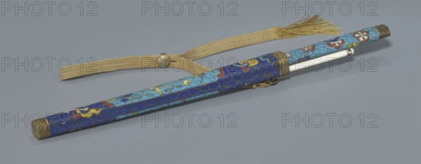 Travel cutlery set in case; 19th century, China, Qing dynasty. Knife with cloisonné enamel handle and steel blade; ivory chopsticks with inlaid black lacquer ornament border; file decorated like the chopsticks. Case of cloisonné enamel with bronze fittings engraved at top and bottom, interior lined with wood; chopsticks and file held by a band with matching border; narrow cotton-silk strap with fringes attached. Case decorated with flowers in two reserves and plant tendrils in the background. Plant motifs and swastika iconography. Cutlery length: 28 cm case., Chinese art; knives, chopsticks., A long cylindrical case with a decorative surface lies on a flat background, accompanied by a woven strap with a round metal fastener and a fringed end. The case features ornate swirling patterns and floral motifs in shades of blue, turquoise, red, yellow, and gold, with metal end caps and a metal collar at one end. A smooth white rod extends partially from one end of the case, and a small decorat...