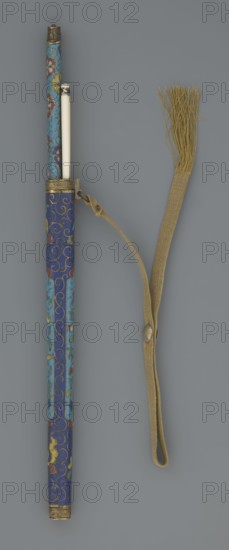 Travel cutlery set in case;, 19th century, China, Qing dynasty. Includes: a Knife with cloisonné enamel handle and steel blade; b–c Ivory chopsticks decorated with an inlaid black lacquer ornament at the top in the form of a border; d File decorated similarly to the chopsticks; e Case made of cloisonné enamel with bronze fittings decorated with engraved ornamentation at top and bottom, interior lined with wood. Chopsticks and file are held by a band decorated with a similar border. A narrow cotton-silk strap with fringes is attached to the case. Case decorated with flowers in two reserves and plant tendrils in the background. Cutlery; plant motifs; swastika iconography. Length: 28 cm case., noted., A slender cylindrical object with a decorative outer case in shades of blue, turquoise, red, yellow, green, and gold, featuring swirling patterns and floral-like motifs, partly open to reveal a smooth pale inner rod; a beige woven strap with a loop and a button-like fastener is attached near...