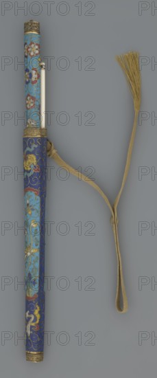 Travel cutlery set in case; Chinese; Qing dynasty 1644–1911; 19th century. Includes: a Knife with cloisonné enamel handle and steel blade. b–c Ivory chopsticks, decorated with an inlaid black lacquer ornament at the top in the form of a border. d File decorated similarly to the chopsticks. e Case 3/4 the height of the cutlery made of cloisonné enamel with bronze fittings engraved at top and bottom; interior lined with wood. Chopsticks and file are held by a band decorated with a matching border; a narrow cotton-silk strap with fringes is attached. Case decorated with flowers in two reserves and plant tendrils in the background. Materials: cloisonné enamel, ivory, steel, bronze, lacquer; function: cutlery; length: 28 cm case., A long cylindrical object with decorative patterns sits vertically against a neutral gray background, showing a top section with a lighter blue surface patterned with floral motifs in red, white, and purple and a lower section in a deeper blue with swirling gold d...
