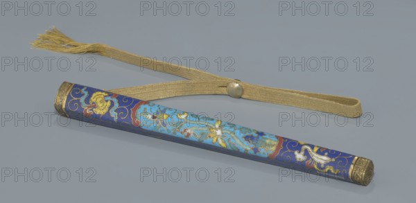 Travel cutlery set in case; Chinese, Qing dynasty 1644–1911, 19th century. Includes: a Knife with cloisonné enamel handle and steel blade. b–c Ivory chopsticks decorated at the top with an inlaid black lacquer ornament in the form of a border. d File decorated similarly to the chopsticks. e Case 28 cm of cloisonné enamel with bronze fittings engraved at top and bottom; interior lined with wood. Chopsticks and file are held by a band decorated with a matching border; a narrow cotton-silk strap with fringes is attached. Case decorated with flowers in two reserves and plant tendrils in the background. Motifs: plant designs and swastika; function: cutlery., An elongated cylindrical object with decorative enamel work in shades of blue, light blue, red, white, and gold lies on a flat gray surface next to a woven gold-colored strap with a tassel and a round metallic button; the cylinder shows floral and scroll motifs in gold and white on blue backgrounds with detailed gold end caps.