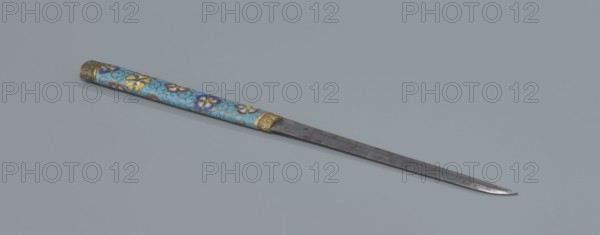 Travel cutlery set in case; Chinese, Qing dynasty 1644–1911, 19th century. Knife with cloisonné enamel handle and steel blade. Ivory chopsticks with inlaid black lacquer ornament at the top in the form of a border. File decorated similarly to the chopsticks. Case reaches 3/4 of the height of the cutlery; made of cloisonné enamel with bronze fittings engraved at top and bottom; interior lined with wood. Chopsticks and file enclosed in a band decorated with a border; narrow cotton-silk strap with fringes attached. Case decorated with flowers in two reserves and plant tendrils in the background. Materials: cloisonné enamel, bronze, steel, ivory, lacquer; function: travel cutlery. Length 28 cm case., A slender metal blade with a tapered point rests on a flat gray surface next to a long decorative handle covered in bright cloisonné enamel featuring a light blue background with floral patterns in yellow, white, purple, red, and dark blue, accented by gold-colored metal fittings at both ends;...