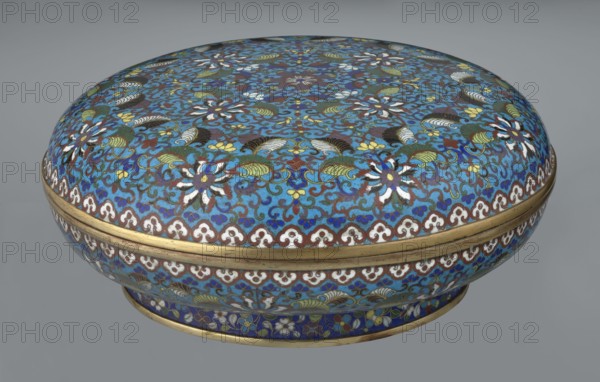 Box with lid, cloisonné enamel, Chinese, Qing dynasty, Qianlong period, 18th century. Large cylindrical-spheroidal box on a separate annular foot with a slightly flattened lid. Surface covered by a plant tendril encircling the container and lid, dominated by chrysanthemum flowers and leaves in various stylistic forms against a turquoise background. Upper edge of the storage section and lower edge of the cover decorated with a ruyi-head border in white and red; a blue three-petal pattern completes the decoration. Foot has an ornamental band of colorful flowers and leafy twigs. Interior of the box and inner surface of the foot filled with uniform turquoise enamel. Unglazed edges of the storage section, cover, and foot are gilded. Height 14.5 cm; diameter 34.5 cm., Function: container., A rounded decorative box with a domed lid sits against a neutral gray background, covered in an intricate floral and foliate pattern in bright blue, turquoise, dark blue, white, green, yellow, brown, and h...
