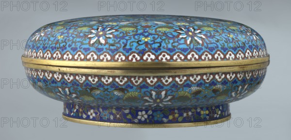 Box with lid, Chinese, Qing dynasty, Qianlong period, cloisonné enamel, 18th century. Large cylindrical, spheroidal box supported on a separate annular foot with a slightly flattened lid. Covered by a plant tendril encircling the entire surface container and lid, dominated by chrysanthemum flowers and leaves in various stylistic forms, set against a turquoise background. Upper edge of the storage section and lower edge of the cover decorated with a ruyi-head border in white and red; a blue three-petal pattern completes the decoration. Foot with an ornamental band of colorful flowers and leafy twigs. Interior of the box and inner surface of the foot filled with uniform turquoise enamel. Ungilded edges of the storage section, cover, and foot are gilded. Function: container. Height 14.5 cm; diameter 34.5 cm., An oval lidded container with a domed top and a short cylindrical base, decorated with intricate floral and scroll patterns in bright blue, turquoise, white, green, yellow, brown, an...